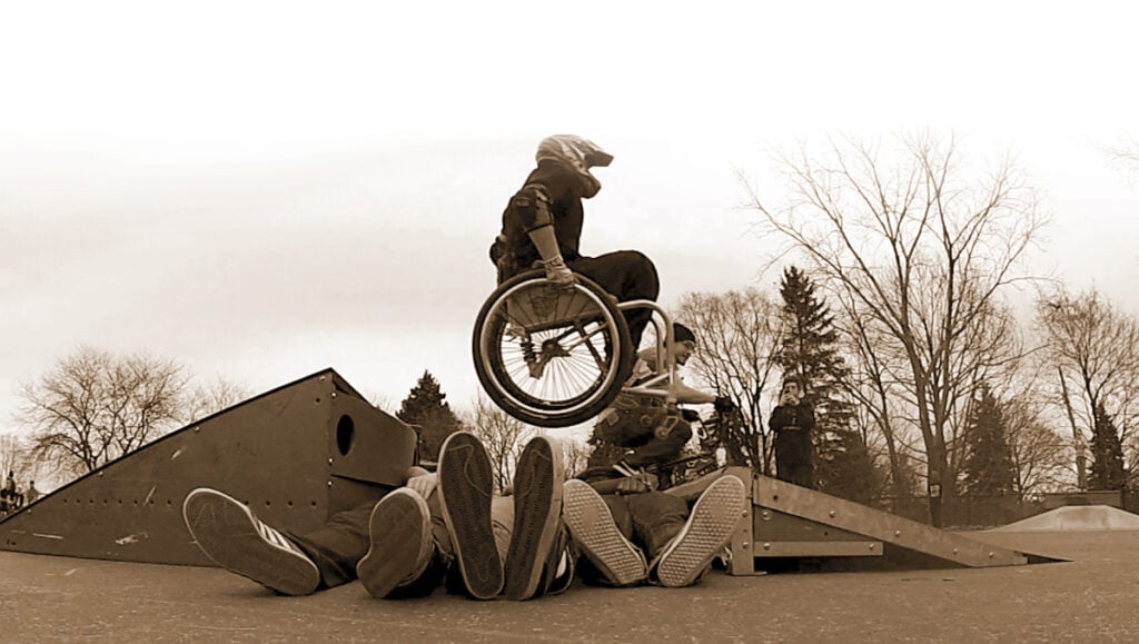 man jumping ramp in a wheelchair over people laying on the group