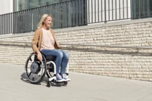 shows woman in manual wheelchair with power assist wheels rolling down a concrete ramp