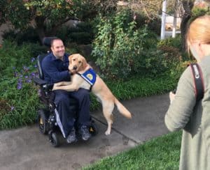 Show man in power wheelchair being photographer with service dog on his lap