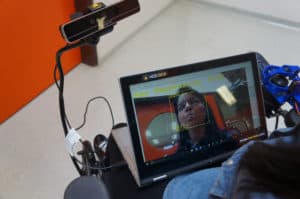 Tablet mounted on wheelchair shows woman who is driving chair using facial expressions