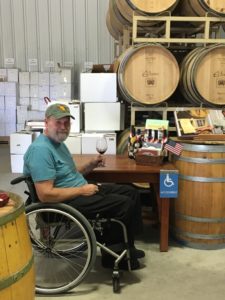 Man in wheelchair and the healing power of wine. he sits in a baseball at a table with wine glass in his hand, surrounded by barrels