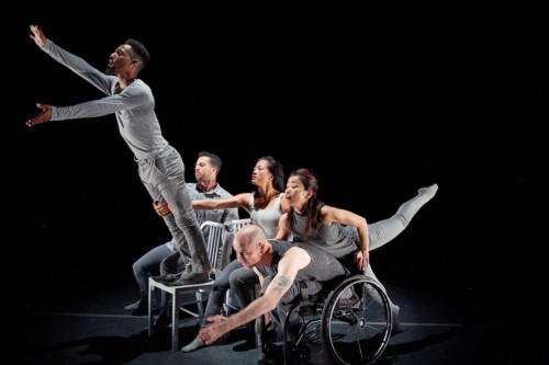 A group of dancer, all in gray hold poses reaching forward