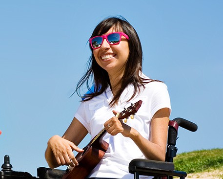 Reveca Torres smiling sitting in wheelchair wearing sunglasses and playing ukulele