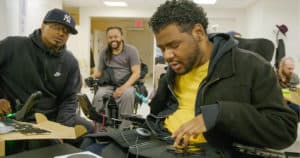Three Black men with quadriplegia are having fun playing adaptive video games.