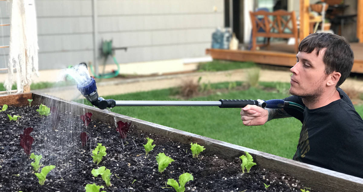 Riley balances the watering wand on his arm in order to maintain control of it. Watering with the wand upside down mimics rain and can keep young plants from being washed out.