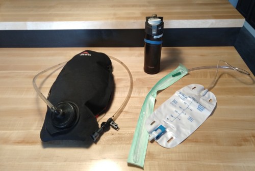 Wood counter with portable coffee thermos, black hydration bladder with drinking spout and catheter, extension tube, leg bag setup