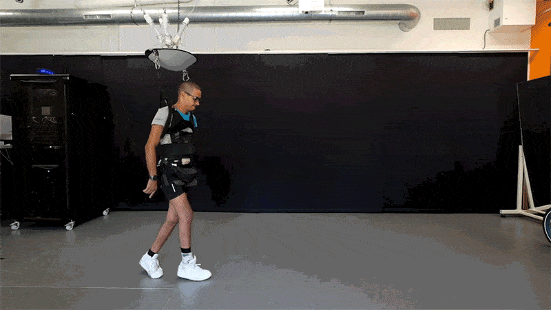 A gif of a young man, walking with the assistance of a harness in a laboratory