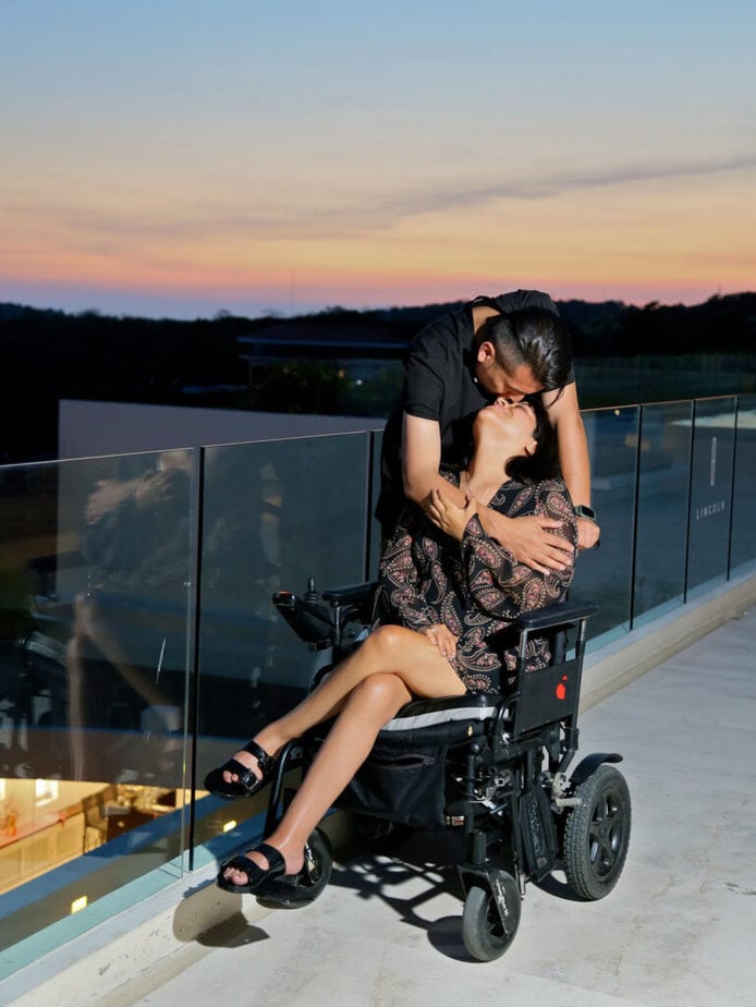 man kissing woman in powerchair on forehead