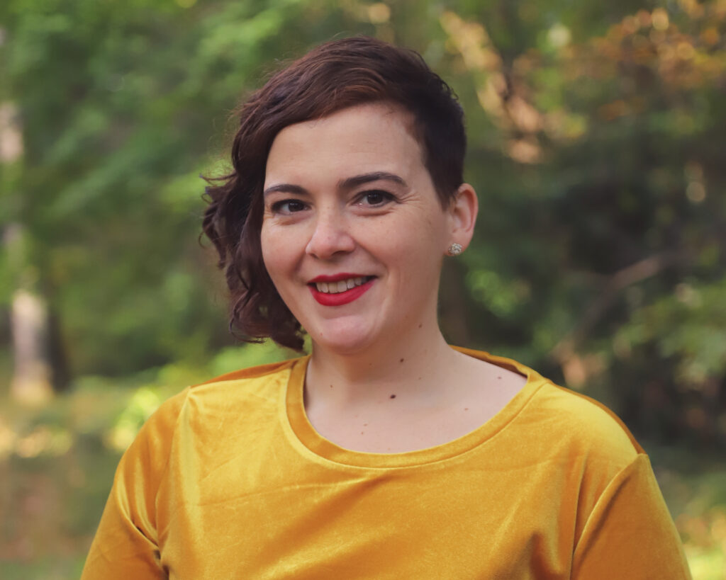 Shows Annie Tulkin, a white woman with brown hair smiling at the camera, wearing a yellow shirt.