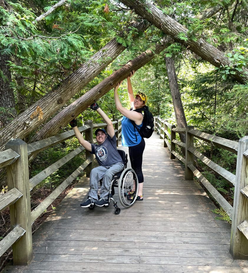 woman standing next to man in wheelchair on a wooden bridge