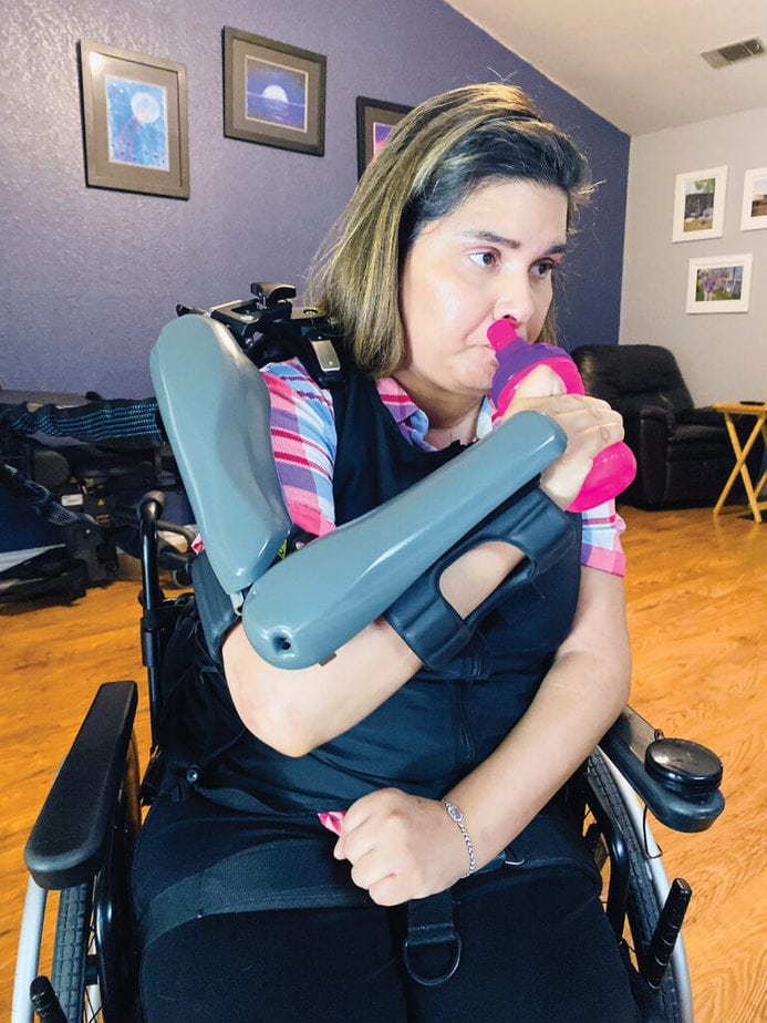woman in wheelchair wearing orthotic device on arm drinking from water bottle