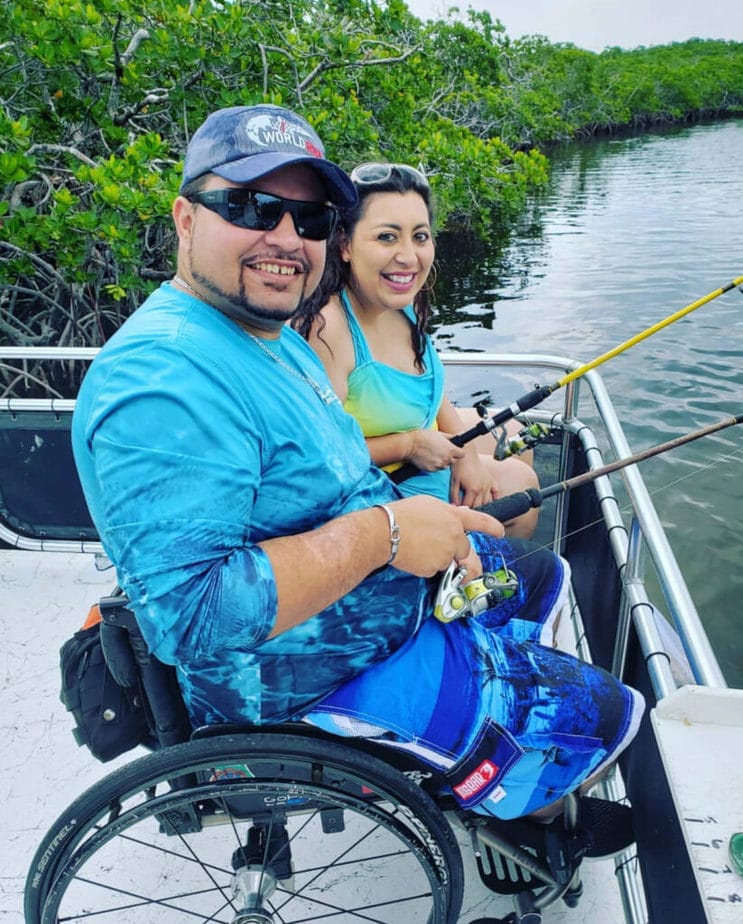woman sitting next to man in wheelchair fishing off a dock