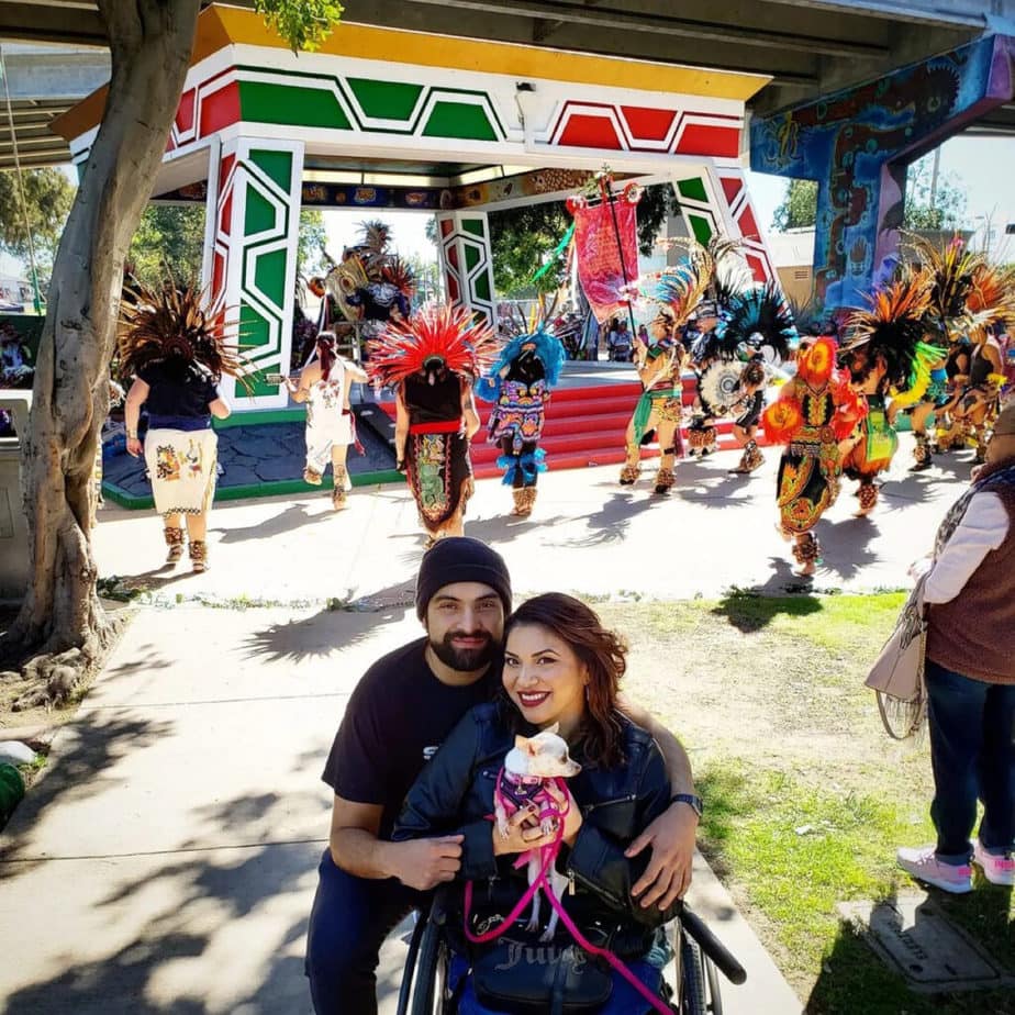 man with arm around woman in wheelchair holding small dog