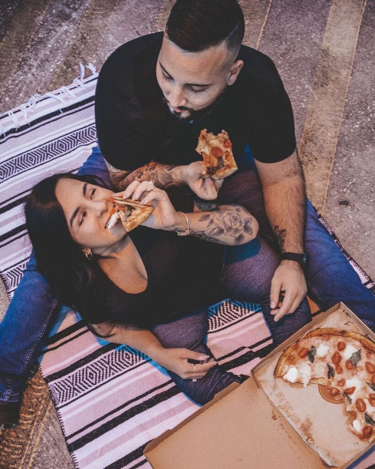man and woman eating pizza on a blanket