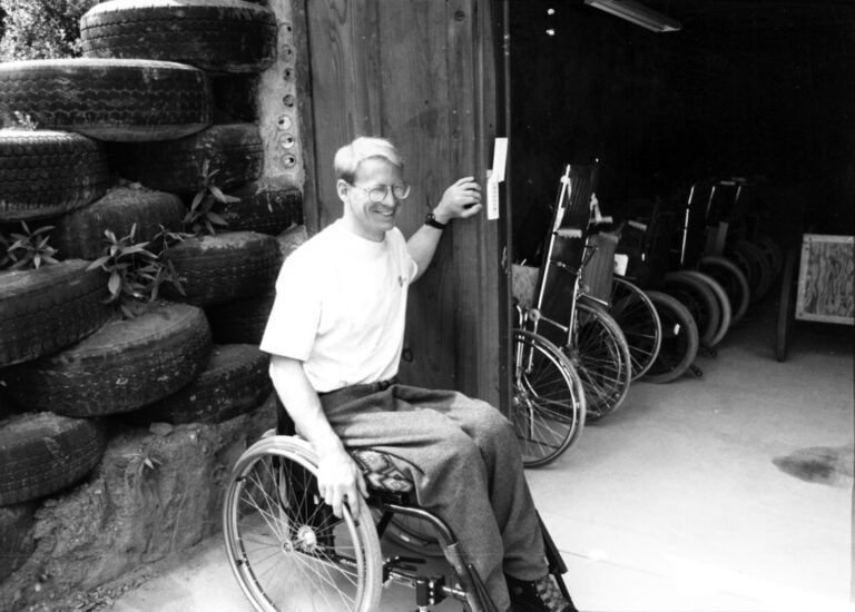 Man in wheelchair sitting in front of a row of old wheelchairs