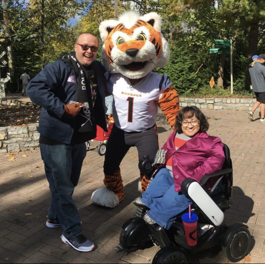 Woman in power wheelchair smiling next to Bengals team mascot and smiling man in sunglasses