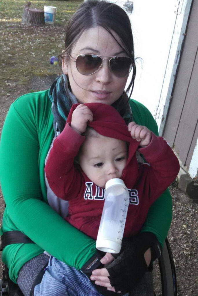 woman in wheelchair outdoors holding baby on lap