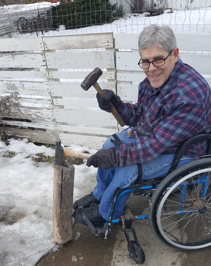 man in wheelchair splitting wood in the snow