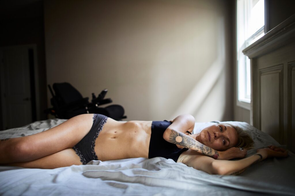 shows white, blond woman, Kelsey Peterson, lying in bed wearing black underwear and bra.