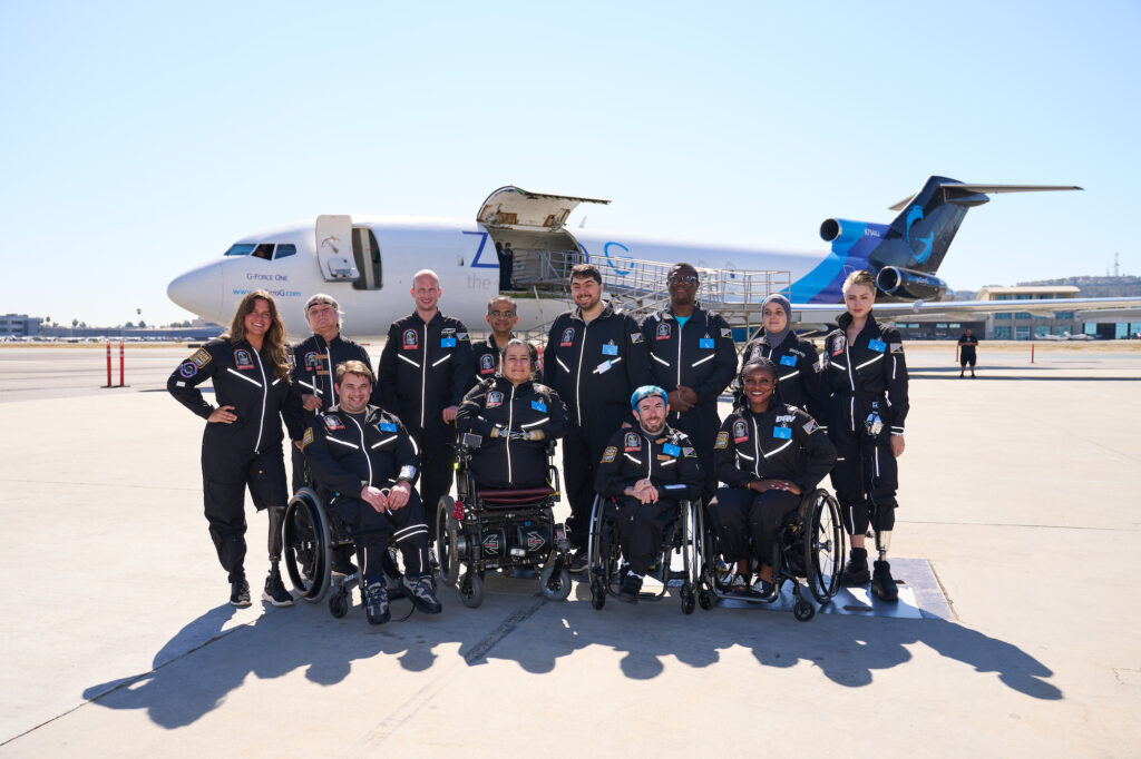 shows 12 people posing in front of a plane, all are wearing blue jump suits.
