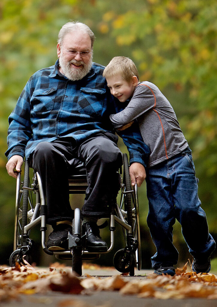 young boy hugging smiling man in wheelchair