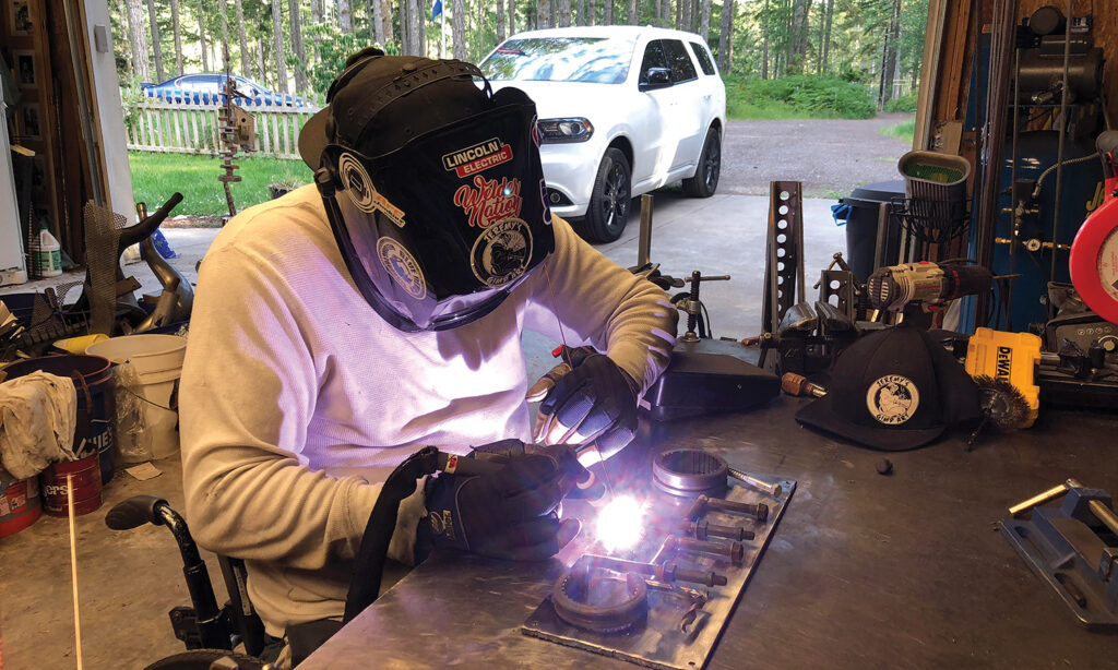 man in wheelchair wearing welders mask and gloves while welding in a garage