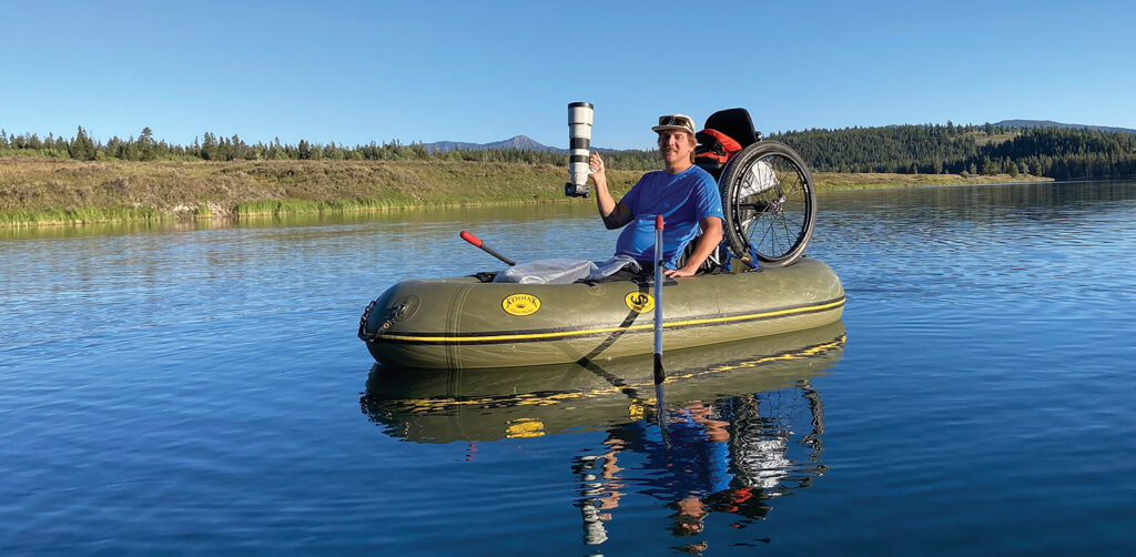 man on water in raft folding long lens camera with wheelchair onboard