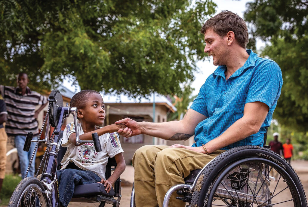 man in wheelchair shaking has with small boy on handcycle in Tanzania