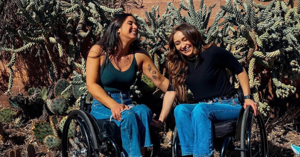 two women in wheelchaurs outdoors laughing