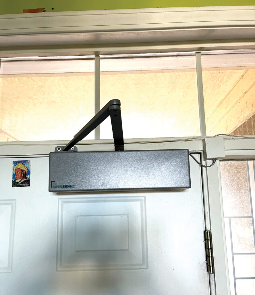 Open Sesame Door Opener unit shown installed at top of door