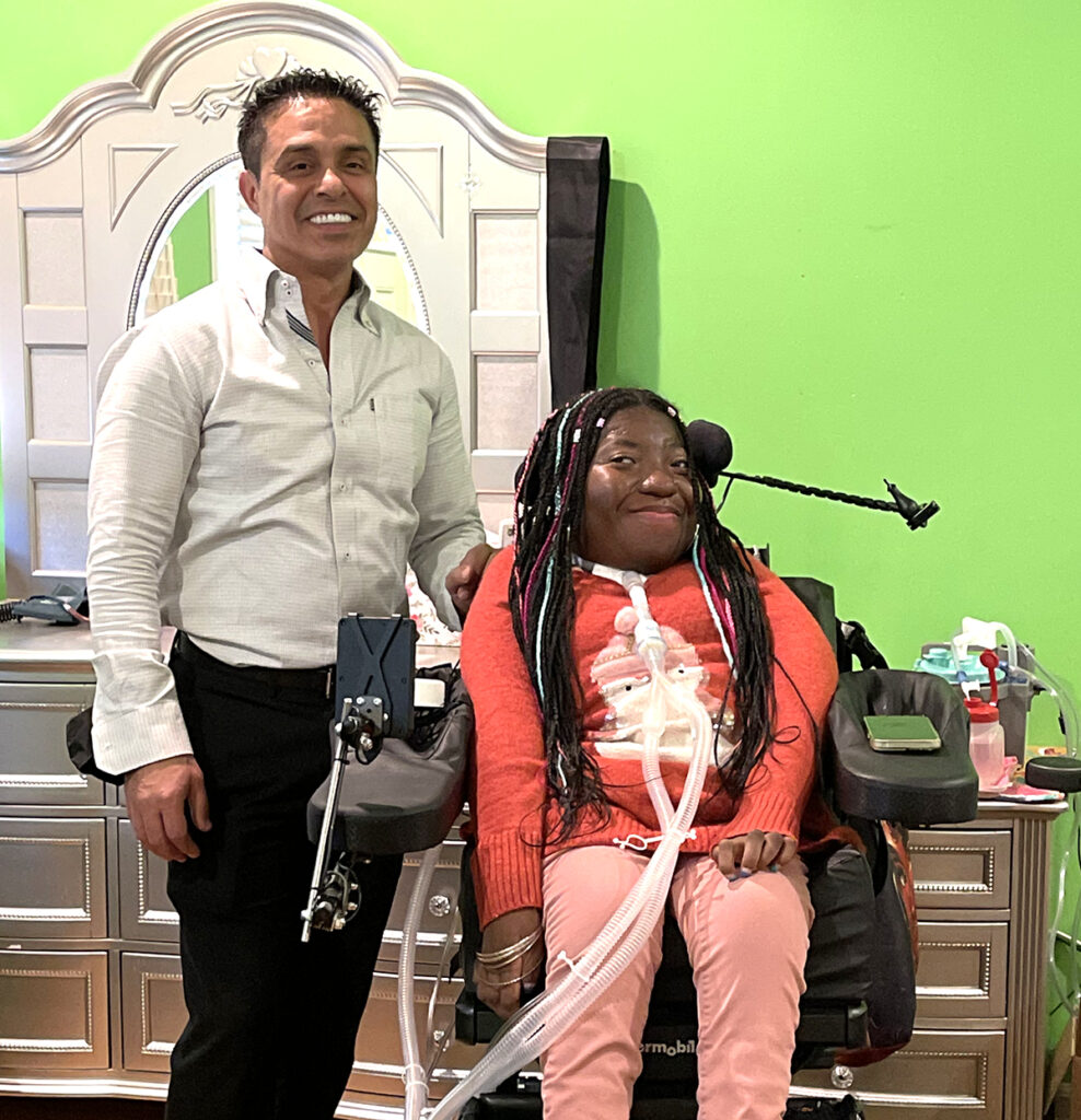 man standing next to young woman in powerchair, both smiling for the camera