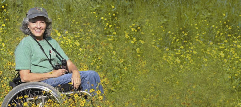 woman in wheelchair in green field with binoculars around neck