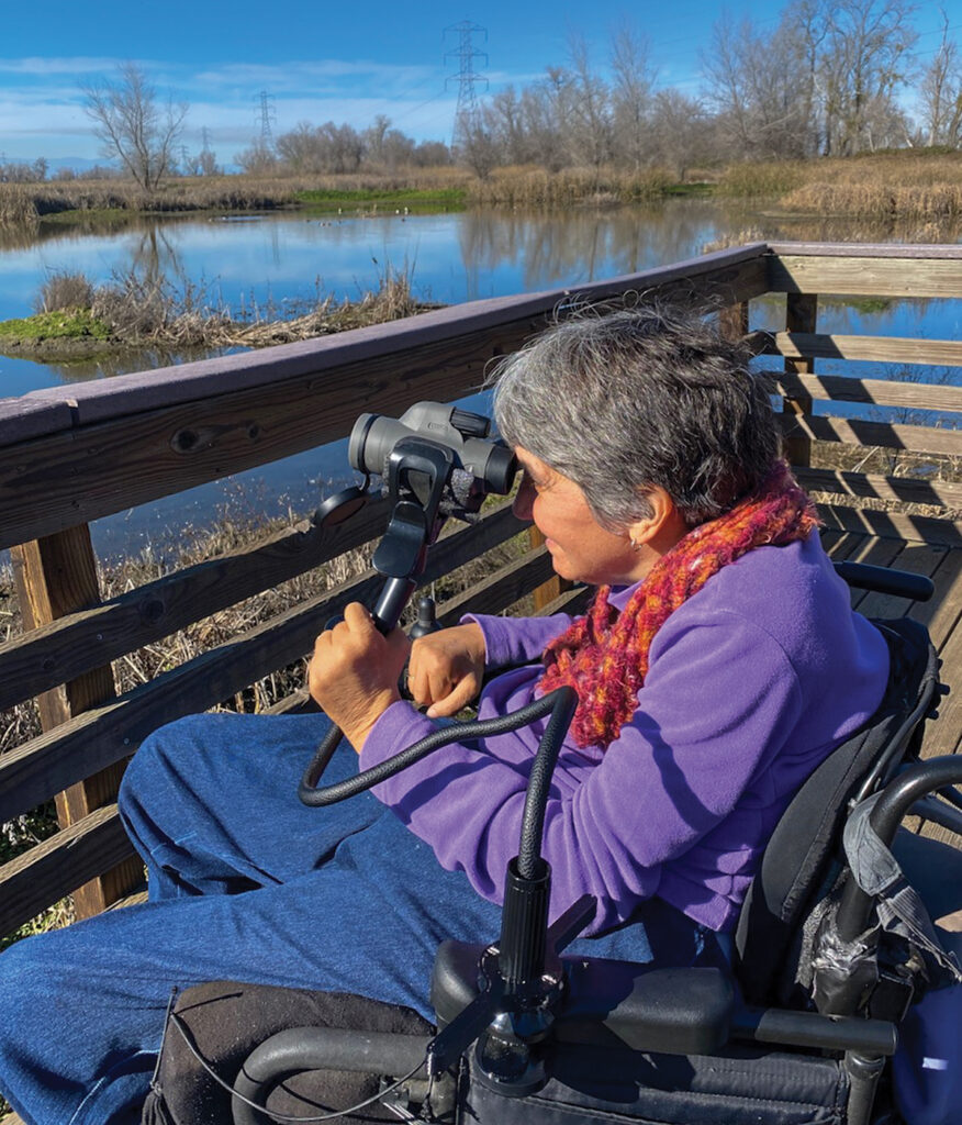 woman on viewing platform looking through binoculars that are attached to her wheelchair