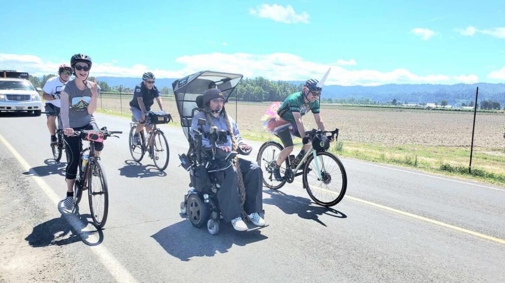 Power wheelchair user on road flanked by bicycle riders.