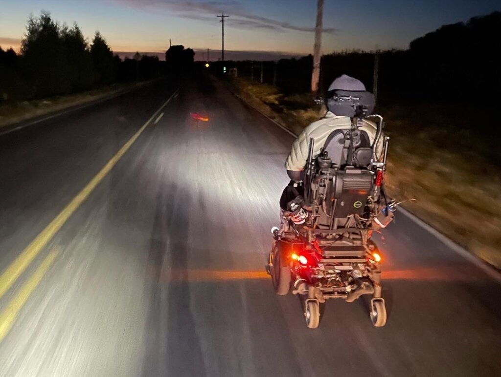 Powerwheelchair user on road at night, seen from behind.