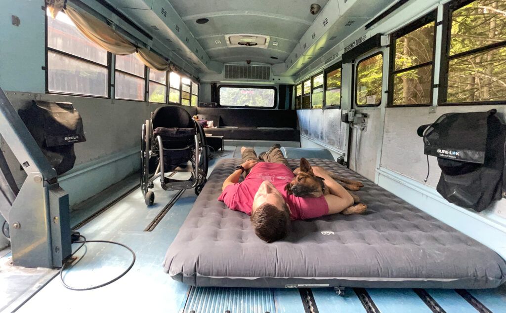 man laying with dog on blow up matress inside a converted bus