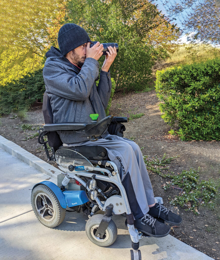 man in powerchair aiming a camera outdoors