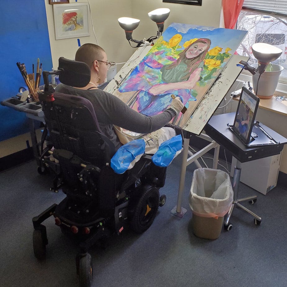 man in powerchair painting a picture of a woman in a wheelchair with dog