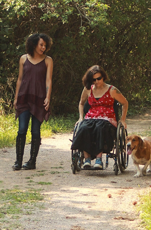 woman and dog walking aise a woman in a whelchair on a dirt path