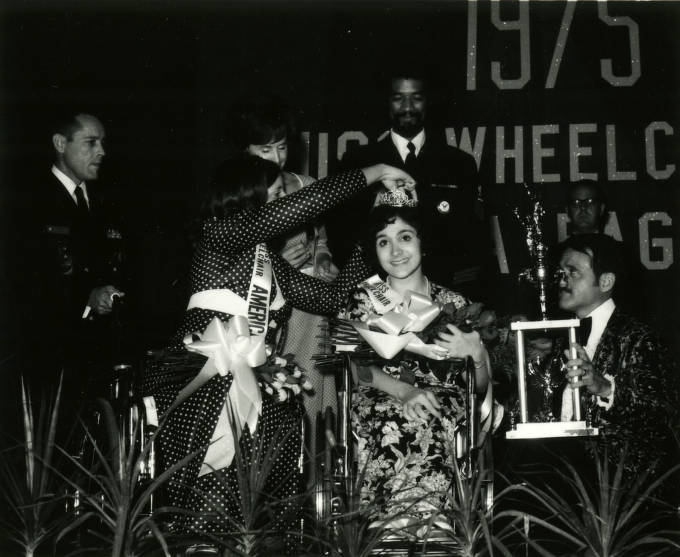black and white photo of woman wheelchair user having crown placed on her head.