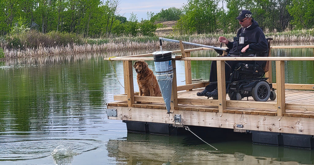 Man in powerchair fishing off a wooden dock with dog watching on