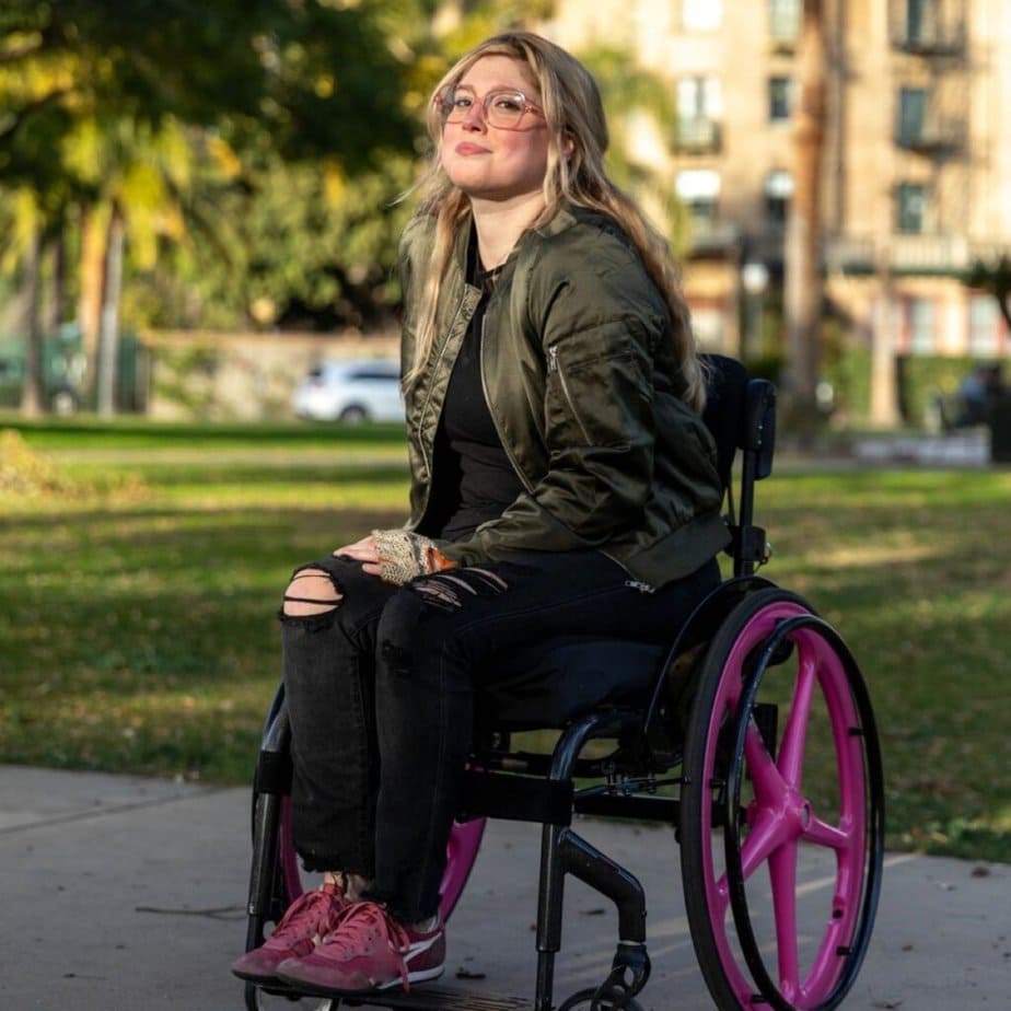 woman in manual wheelchair sitting outside with pink x-core wheels.