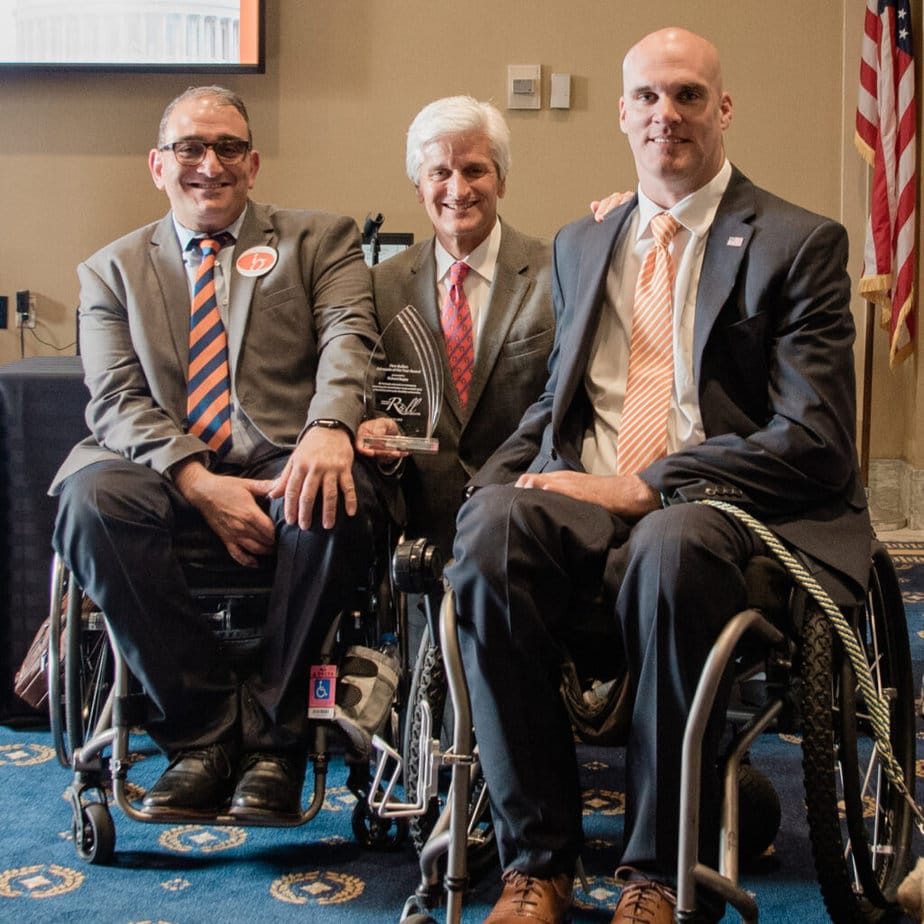 three men in wheelchairs possing for camera in front of US flag
