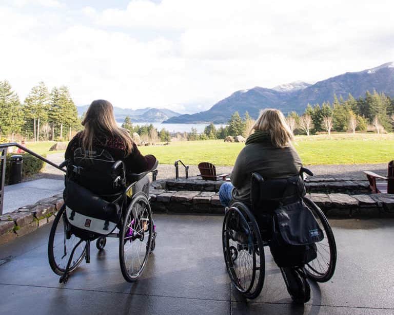 Two manual wheelchair users on concrete patio looking out at view of rivers and mountains