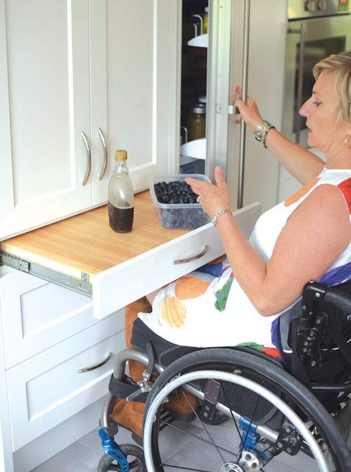 woman in wheelchair using a pull out shelf installed counter height in kitchen cabinets