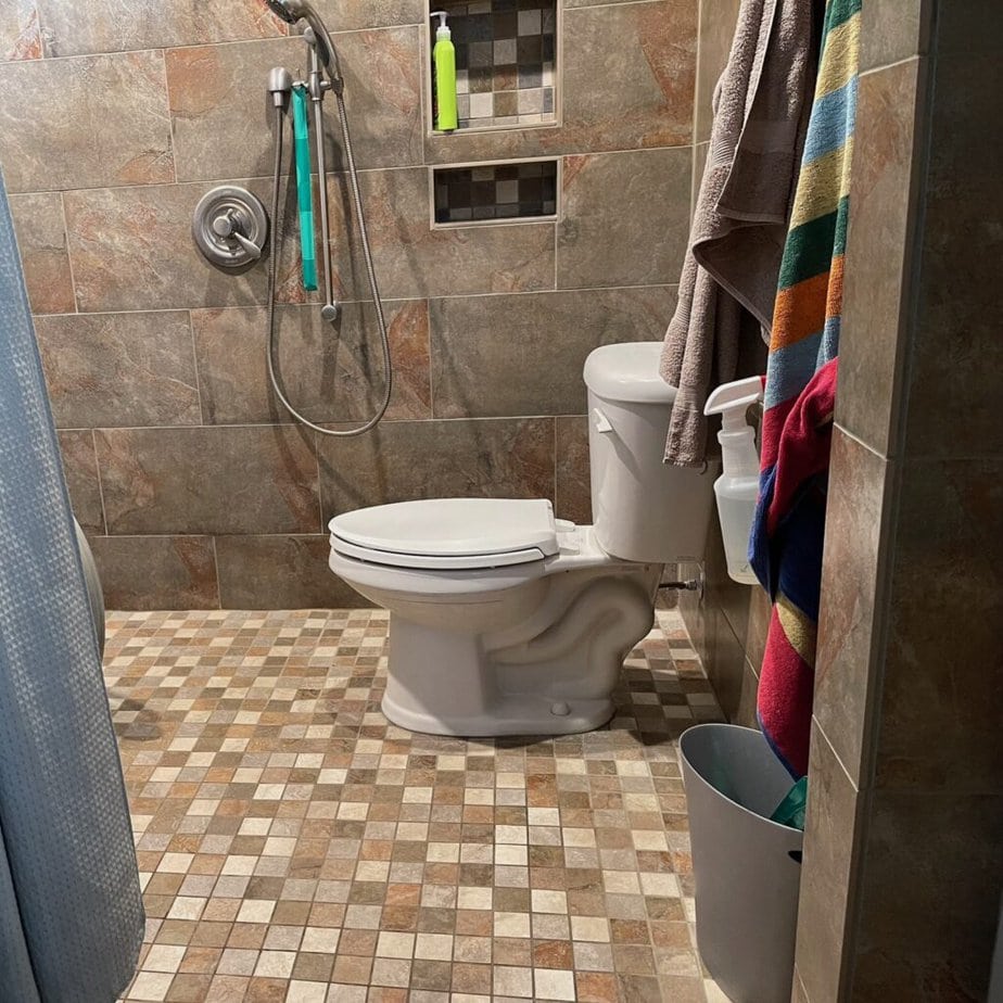 tiled bathroom with roll-in shower and toilet with handheld shower head next to it.
