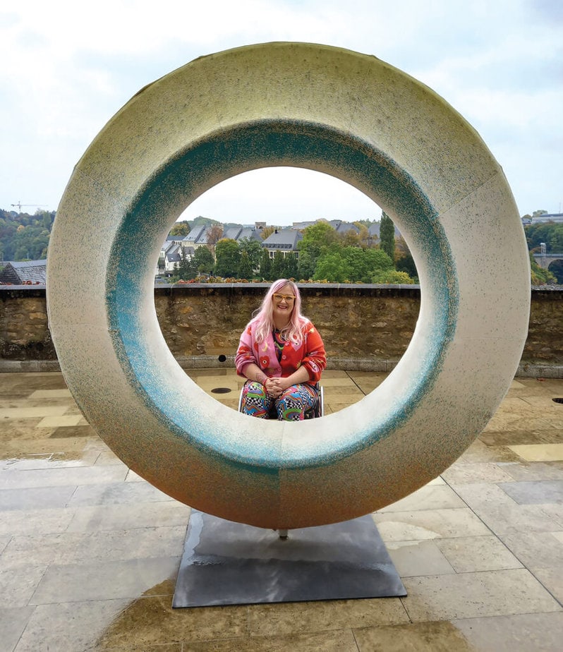 woman in wheelchair pictured behind a circular sculpture with opening in the middle