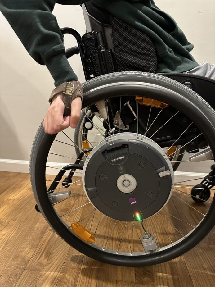 Side profile of manual wheelchair user pushing with gloves.