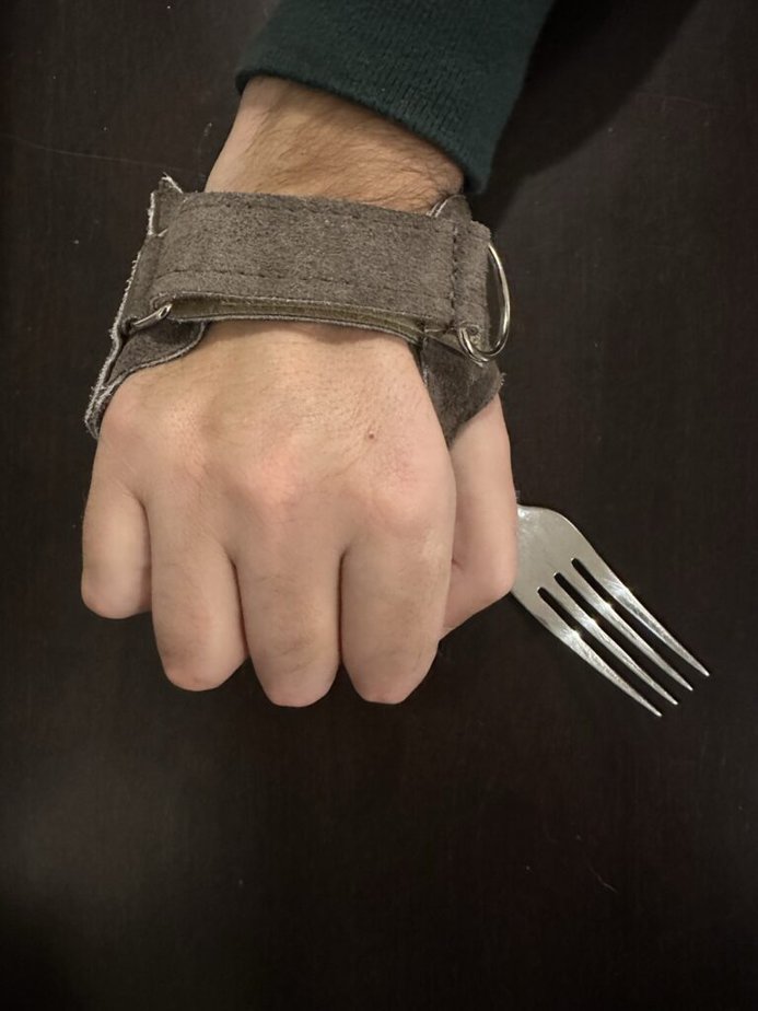 Top of a fist wearing a brown leather glove with a fork tucked in.