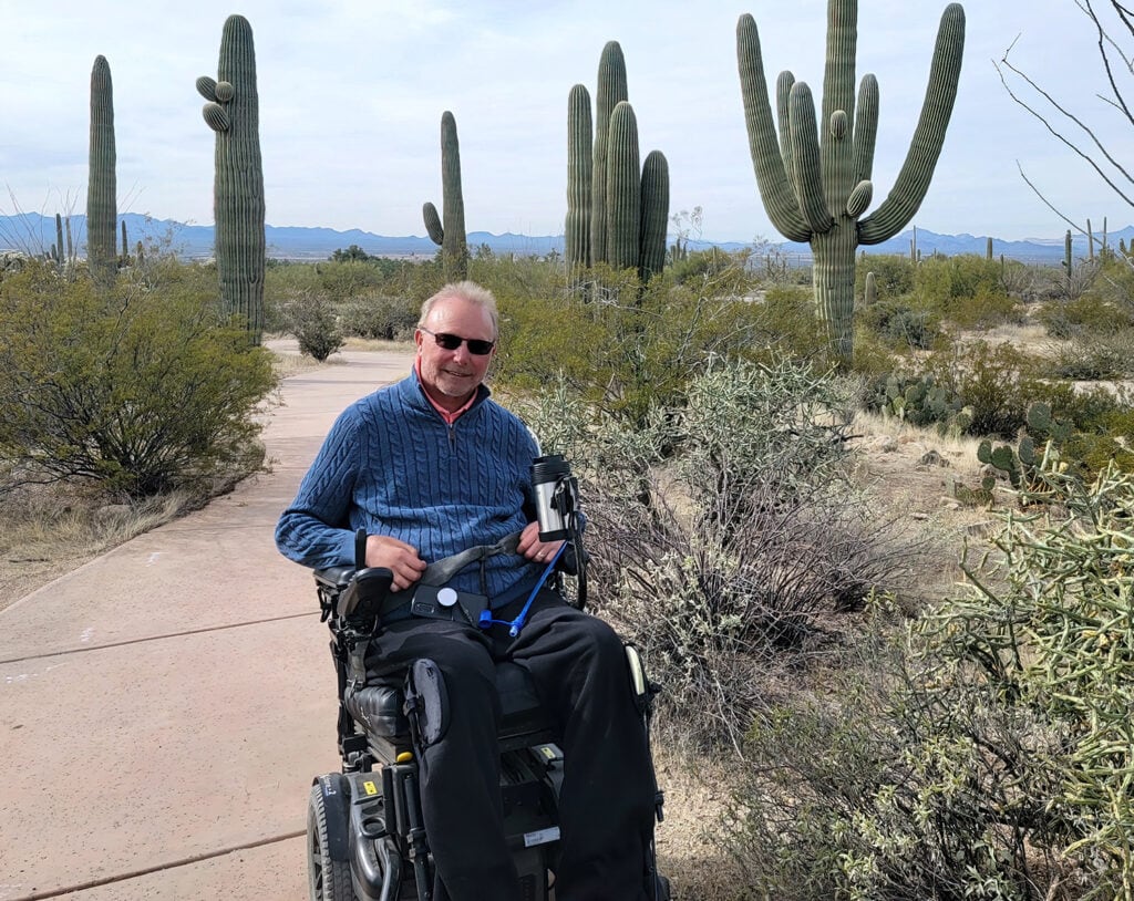 man in powerchair on a path in Arizona dessert with cacti in background